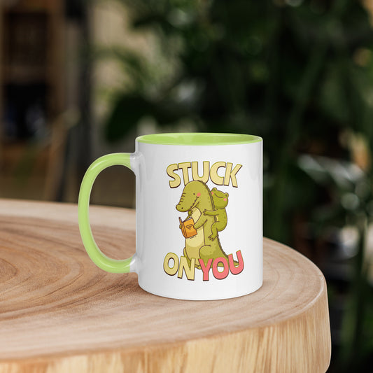 White ceramic mug with green inside featuring a crocodile reading a book and a cute frog hugging it with "STUCK ON YOU" text